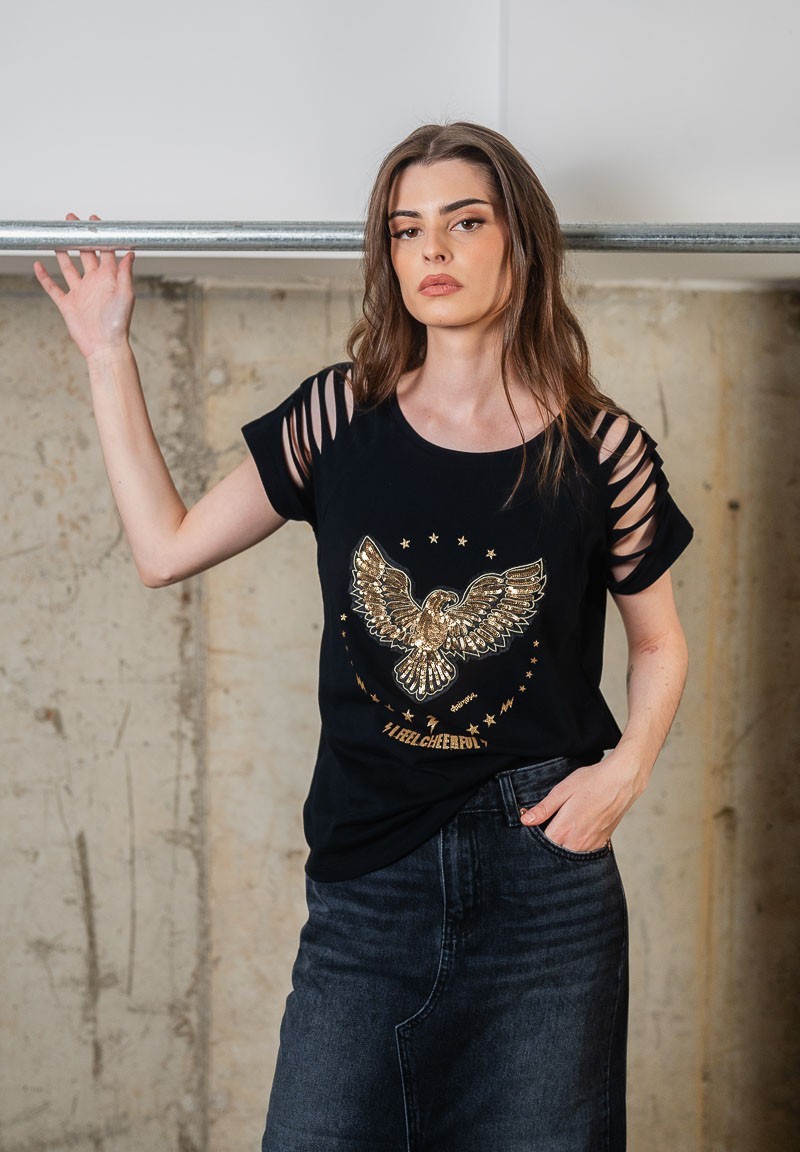 Camiseta negra con aberturas en los hombros y águila de lentejuelas bordada. Plano medio cuerpo.
