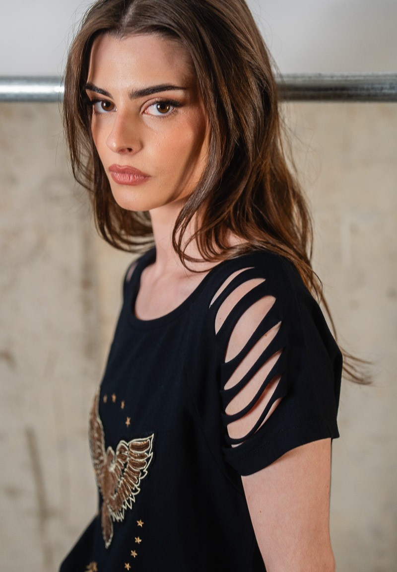 Camiseta negra con aberturas en los hombros y águila de lentejuelas bordada. Detalle aberturas hombros.